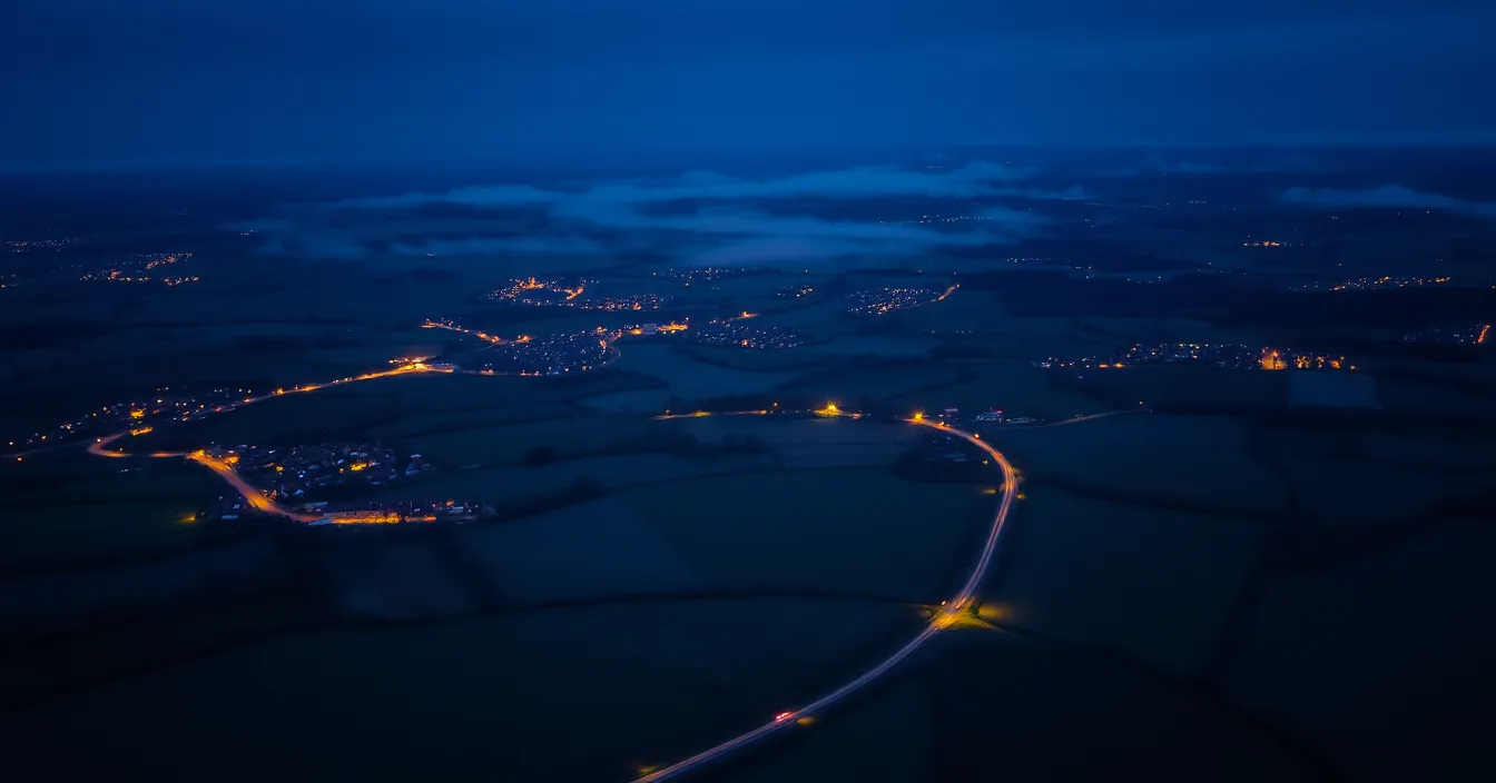 Vue aérienne d'une campagne française à la tombée de la nuit, bourgs éclairés dispersés et routes qui les relient.